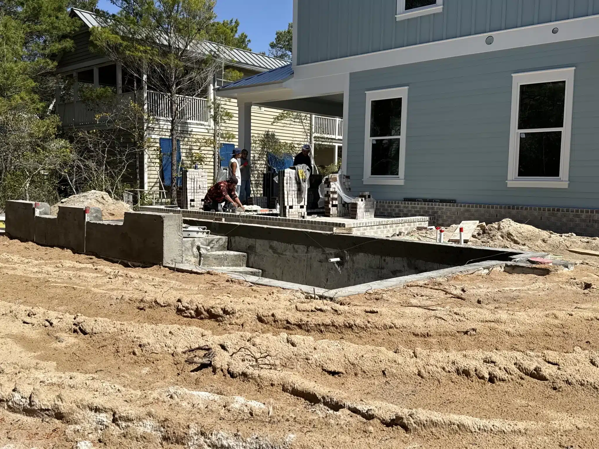 New construction scene: partially built swimming pool and gray house with workers.